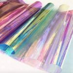 Iridescent Rainbow Film roll by Jeewa Plastic Close-up of Rainbow Film reflecting a spectrum of colors Rainbow Film sheet applied on a craft project showing color shift Flexible Rainbow Film bent to demonstrate pliability Rainbow Film used for eye-catching signage application